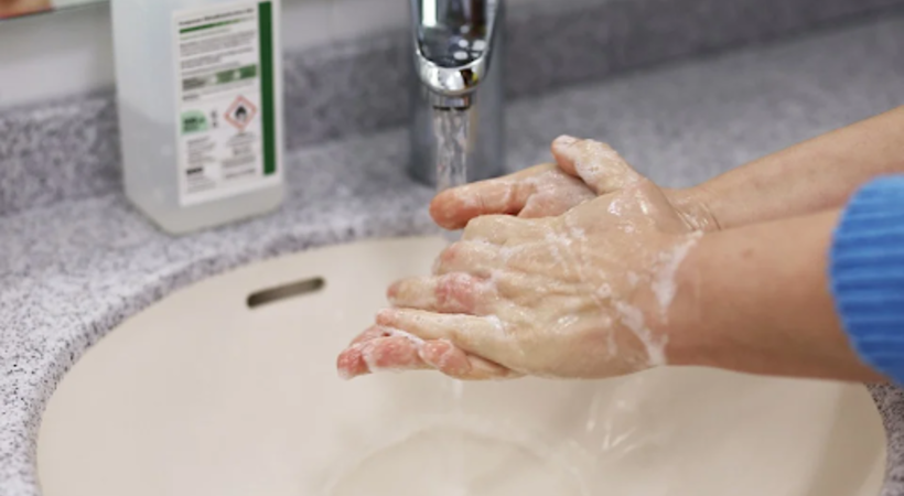 Pessoa lavando as mãos com água e sabão no banheiro da empresa.