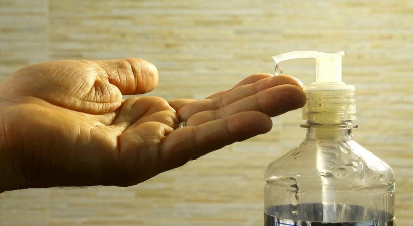 Mão embaixo de um frasco de álcool em gel.