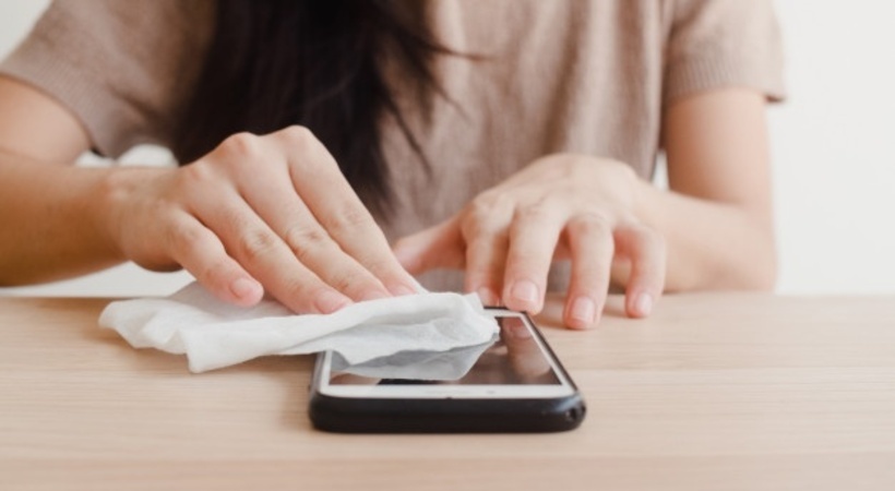 Foto de mulher desinfectando seu aparelho celular com um lenço.  