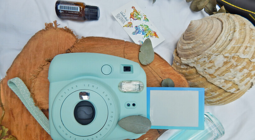 Foto aérea com frasco de óleo essencial, camera fotográfica, elementos relacionados a viagem e um outro franco azul. 