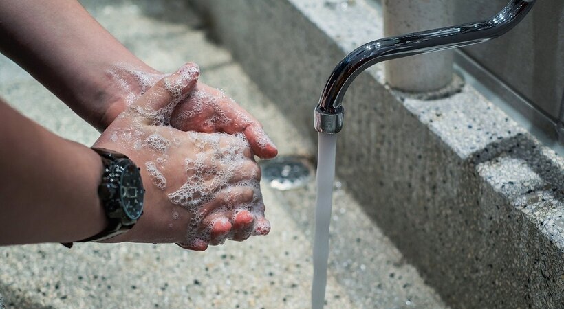 Pessoa lavando as mãos com água e sabão em uma pia.