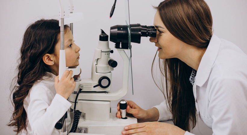 Foto de médica oftalmologista examinando olho de criança com ajuda de equipamento. 