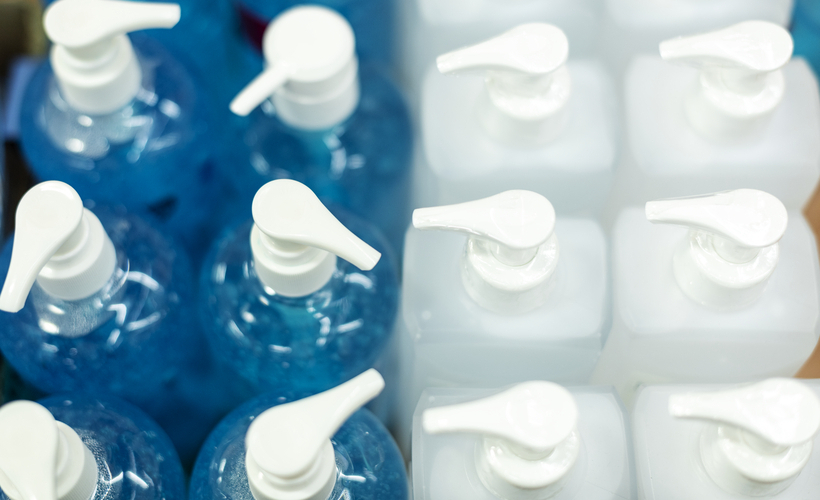 Foto superior de vários frascos de álcool em gel, alguns transparentes e outros de cor azul.