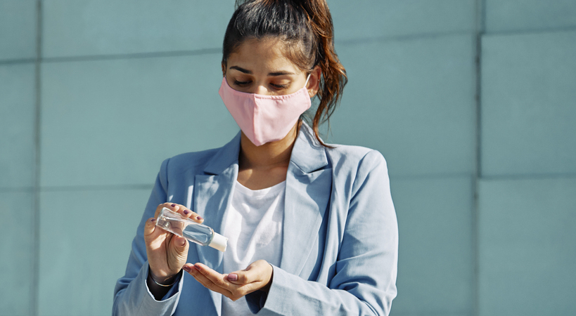 Mulher com máscara usando antisséptico para as mãos durante a pandemia