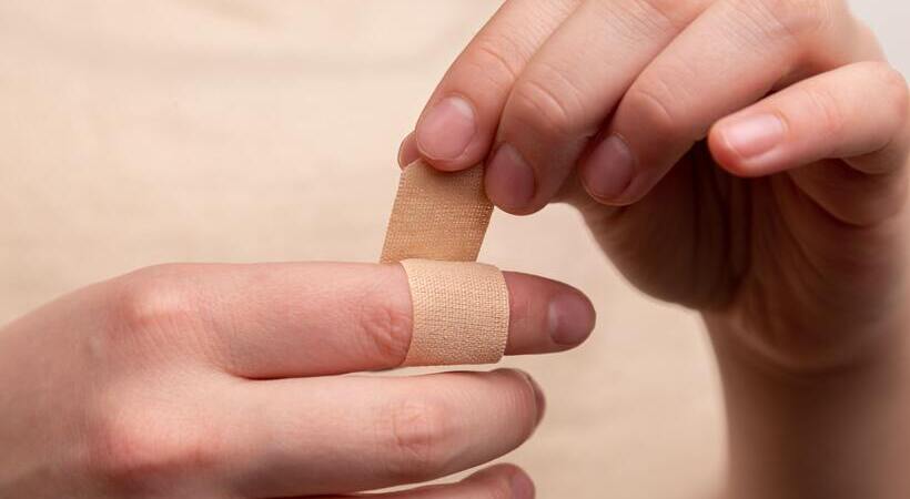 Pessoa colocando um band-aid em dedo. 