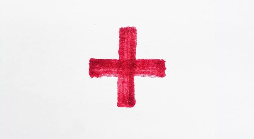 Cruz vermelha pintada em tinta sobre papel branco. 
