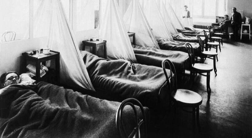 Pessoas em camas de hospitais durante surto de gripe no passado. As divisões dos leitos são feitas com lençóis.