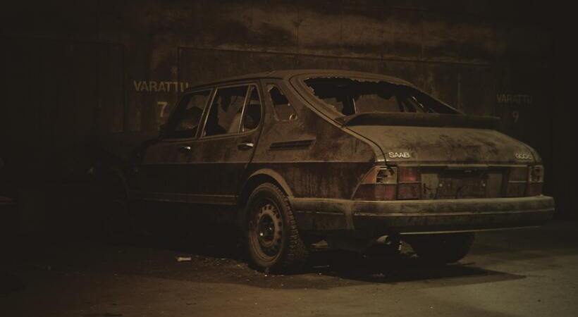 Carro antigo com os vidros quebrados e coberto de poeira em garagem. 