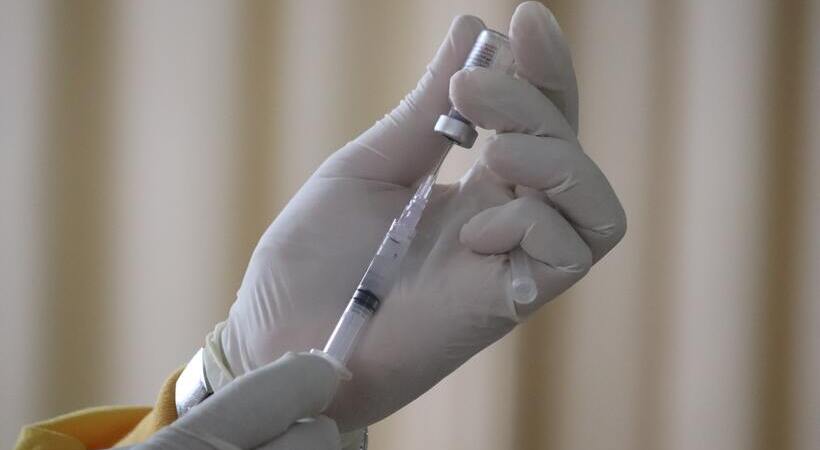 Pessoa com luvas de látex colocando vacina em uma seringa