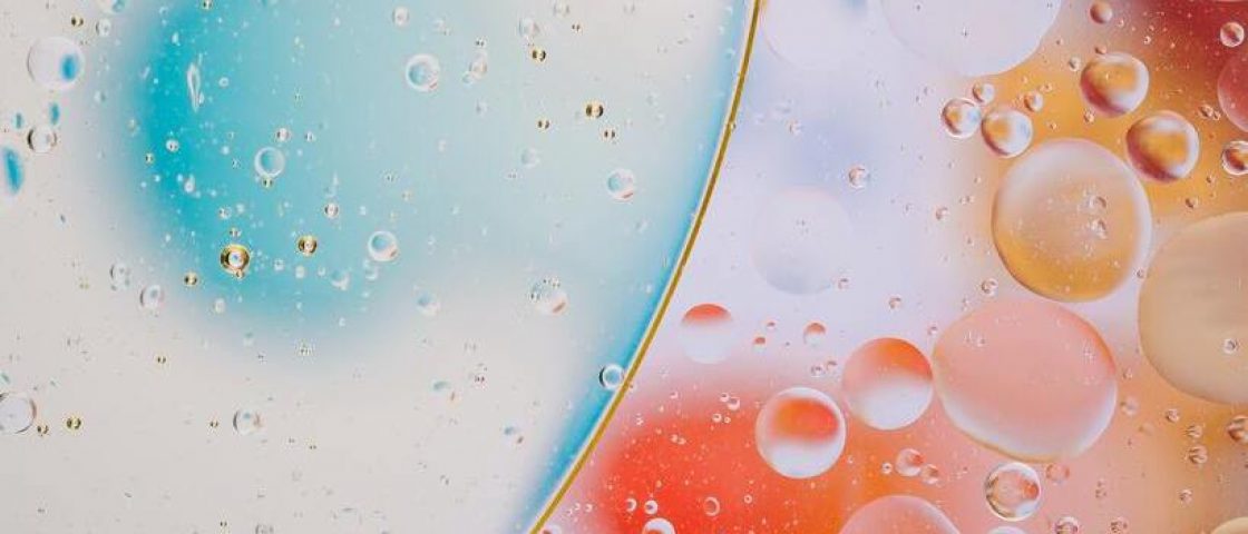 Gotas sobre superfície transparente iluminada com cores que vão do azul ao amarelo e laranja.